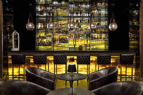 Upscale bar with illuminated shelving, hanging pendant lights, and quilted seating