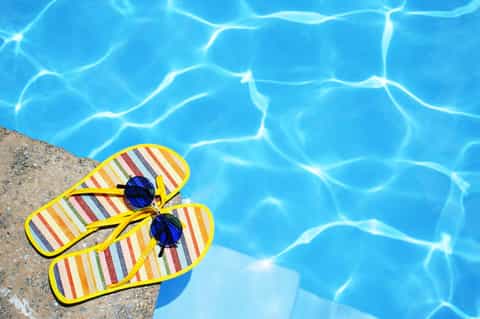 Yellow striped flip-flops and sunglasses resting on pool edge with crystal-clear blue water