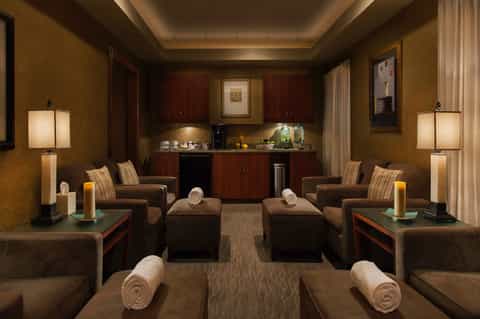 Luxury spa relaxation room with brown leather recliners, dim lighting, and beverage station