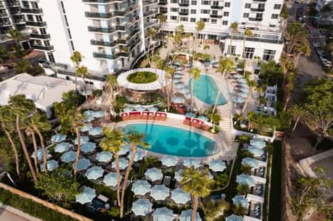 Aerial view of resort complex with two curved pools, lounge chairs, and surrounding hotel buildings