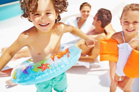Children playing by a resort pool wearing colorful swim floaties with adults supervising in background