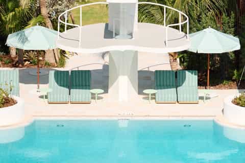 Outdoor pool deck with cabanas, umbrellas, lounge seating, and tropical landscaping