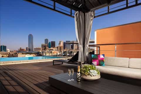 Rooftop terrace with city skyline view, modern lounge seating, pergola with curtains, and turquoise pool