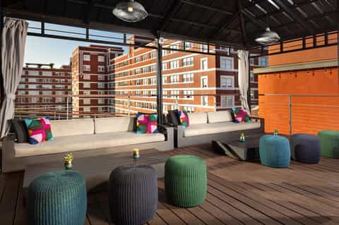 Rooftop lounge with modern seating, colorful pillows, and urban cityscape views