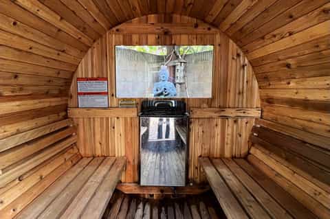 Wooden barrel-shaped sauna interior with benches, wooden construction, and glass viewing window