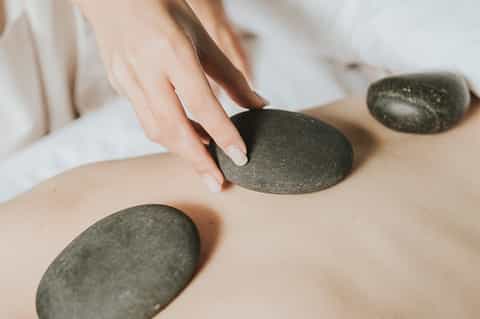 Close-up of hot stone massage therapy with person's hands placing smooth basalt stones on client's back