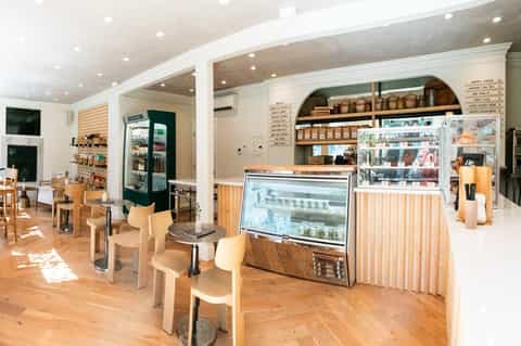 Bright café interior with wooden furniture, refrigerated display case, and open shelving