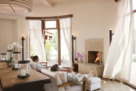 Spa relaxation room with fireplace, cream seating, flowing white curtains, and ocean view doors