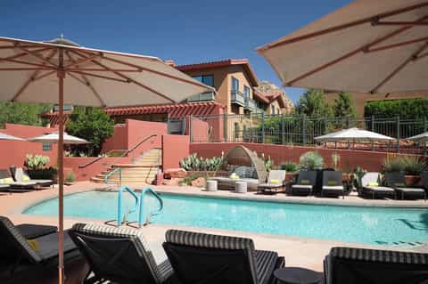 Resort pool with turquoise water, striped loungers under umbrellas, red terracotta building with balcony
