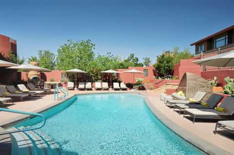 Resort pool with turquoise water surrounded by red terracotta buildings, umbrellas, and desert landscaping