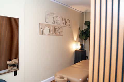 Modern spa treatment room with 'Forever Young' sign and massage table