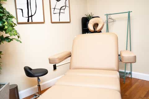 Spa treatment room with cream-colored massage chair, footstool, mirror, plants, and contemporary decor