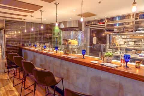 Modern hotel bar with wooden counter, pendant lighting, and stocked shelves