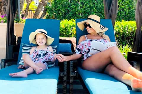 Woman and child relaxing on blue lounge chairs by the pool wearing sun hats