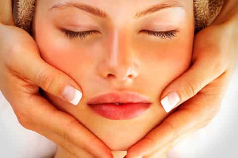 Close-up of woman's face receiving relaxing spa facial treatment with hands massaging temples