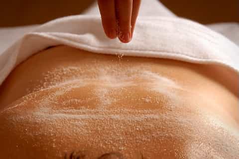 Hand sprinkling sand on person's back during beach spa treatment