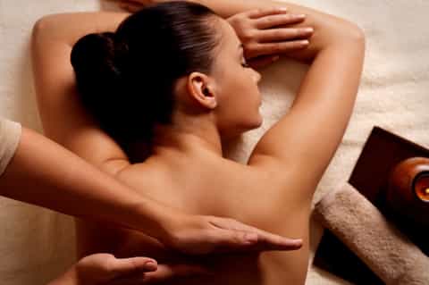 Woman receiving back massage on spa table with towels and wellness products nearby