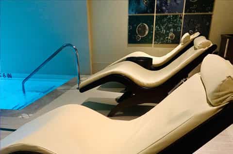 Indoor spa area with white loungers beside illuminated swimming pool