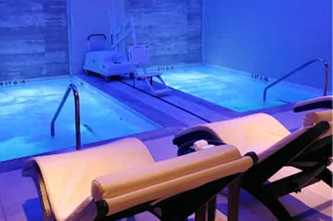 Indoor swimming pool with blue lighting, spa loungers, lap lanes, and underwater illumination