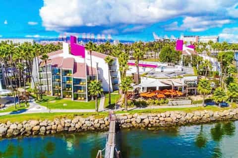 Aerial view of modern waterfront resort with magenta accents, palm trees, and river setting