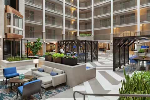 Modern hotel atrium with multiple balconied floors, ground-level lounge seating, and contemporary architecture