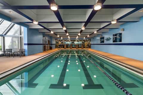 Indoor lap pool with lane dividers, blue water, ceiling lights, and modern athletic facility