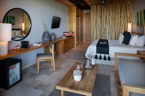 Luxury resort room with king bed, wooden furnishings, mirror, and spa amenities
