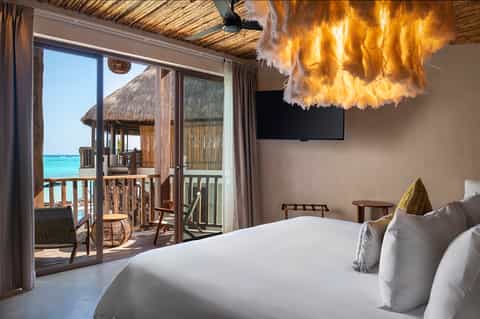 Overwater bungalow bedroom with ocean view, balcony, and tropical decor