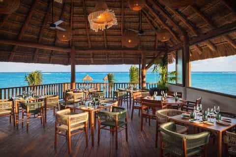 Beachfront restaurant with thatched roof, ocean views, and wooden dining tables