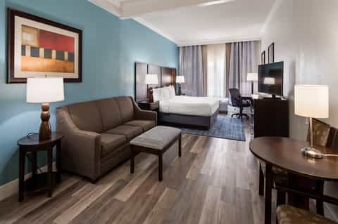 Hotel suite with blue accent walls, sofa, bed, and desk with flat-screen TV