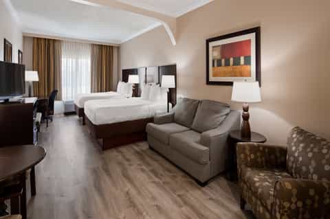Spacious hotel room with two queen beds, seating area, TV, and neutral beige color scheme