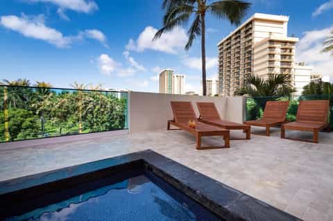 Rooftop terrace with wooden loungers, spa pool, palm trees, and high-rise residential views