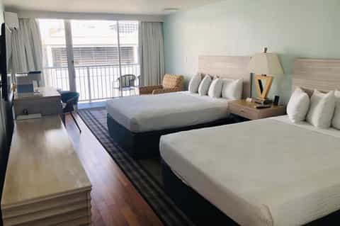 Hotel room with twin beds, ocean balcony view, light blue walls, and modern furnishings