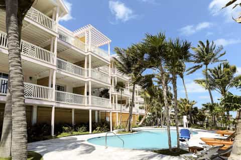 Beachfront resort building with white railings, multiple balconies, pool, and palm trees