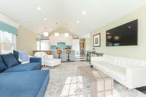 Contemporary living room with blue sofa, white furniture, open kitchen, and bright natural lighting