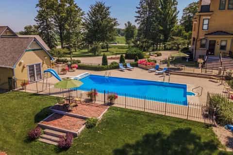 Rectangular backyard pool with slide, fencing, landscaping, pool house, and rural property setting
