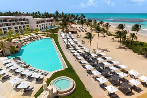 Beachfront resort with pool, lounge chairs, palm trees, sandy beach, and turquoise ocean view