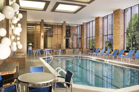 Indoor natatorium with lap pool, blue loungers, decorative lighting, and exposed brick architecture