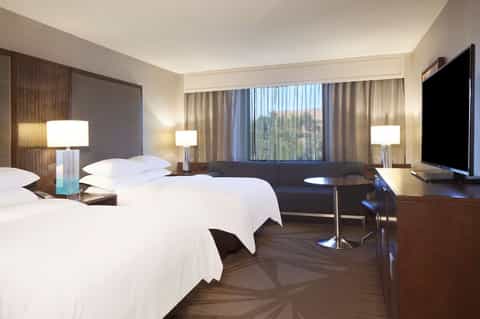 Modern hotel room with two queen beds, wood accents, desk area, and large windows with nature view