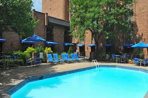 Resort pool with blue umbrellas and lounge chairs against brick building with ivy