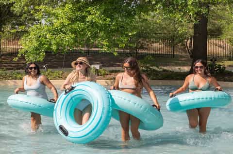 Four women in pool holding turquoise floats with trees and fencing visible in background