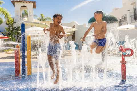 Children playing in splash pad with water fountains at resort courtyard with Spanish architecture
