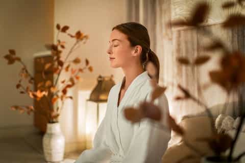 Serene spa room with woman in white robe and dried flower arrangement in natural light