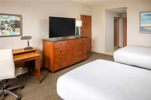 Hotel guest room with two queen beds, wooden dresser with TV, desk lamp, and beige carpeting