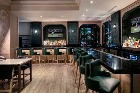 Upscale sports bar with green leather seating, black shelving with liquor bottles, and multiple TV screens