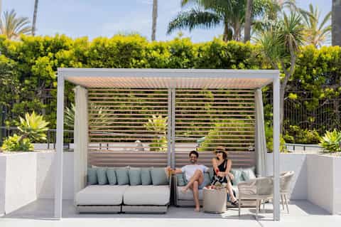 Couple relaxing in modern pergola with gray cushioned seating and tropical landscaping