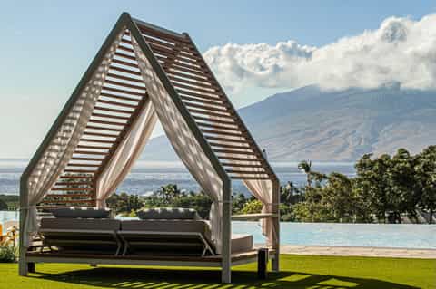 Modern cabana with striped shade structure overlooking infinity pool and mountain lake landscape