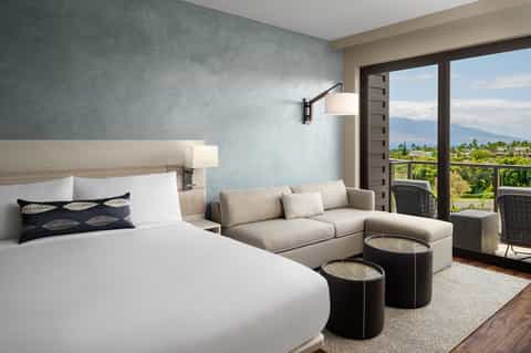 Modern hotel room with bed, sofa, mountain view balcony, and contemporary minimalist design