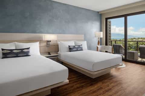 Modern hotel bedroom with two beds, ocean view balcony, and contemporary furnishings