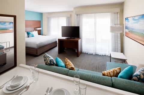 Spacious hotel suite with separate bedroom, living area, turquoise accents, and oceanview balcony